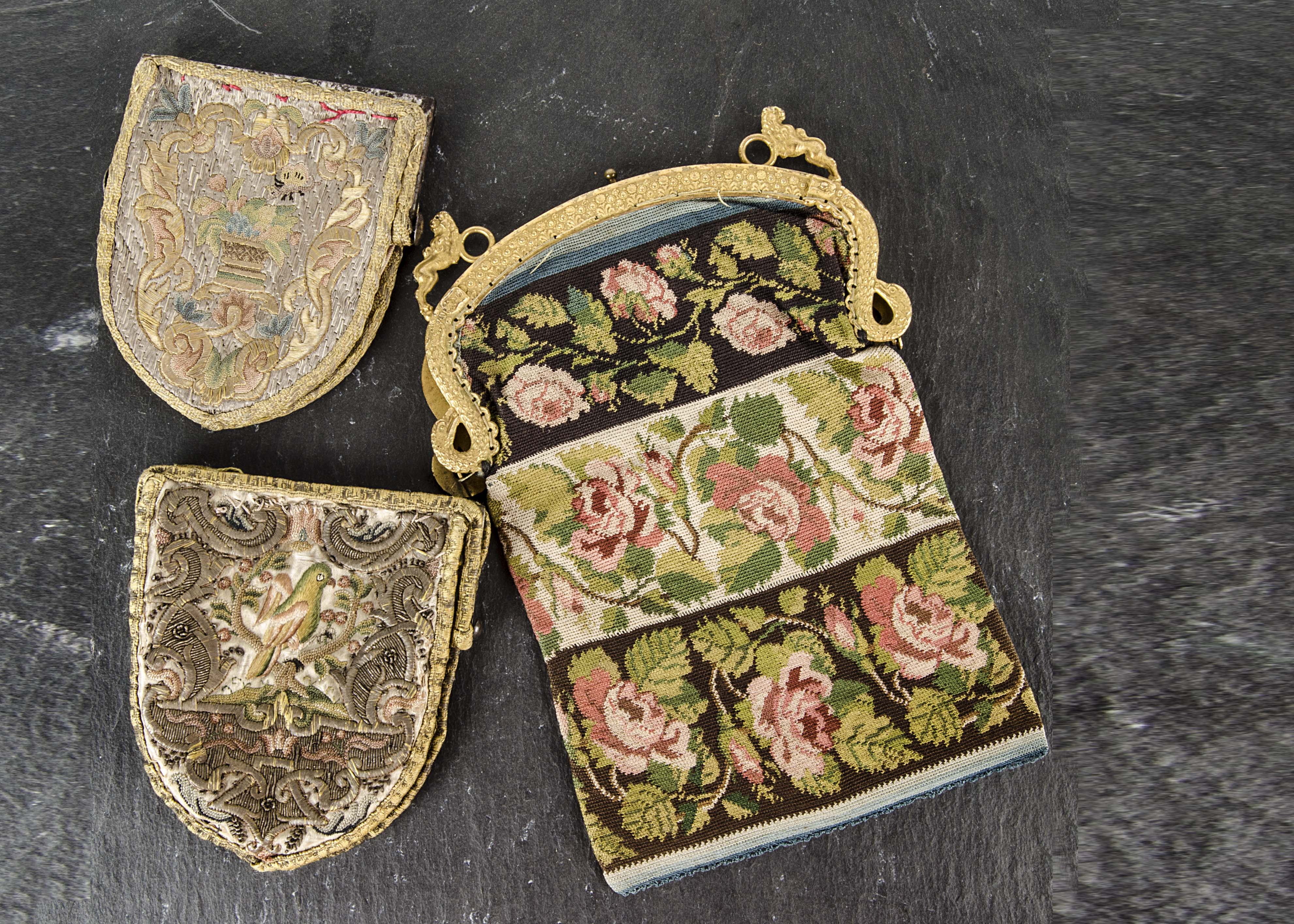 Three embroidered purses, two shield shaped with birds and flowers circa 1790 and a button holed reticule, mid 19th century